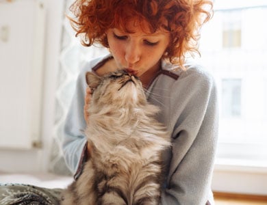 red-haired woman giving a kiss on the head of a long-haired tabby cat