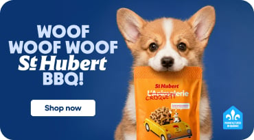 A blue promotional banner features a small corgi puppy centered in the image, holding an orange bag of dog food in its mouth. The bag is branded “St‑Hubert La Croquettière” and shows kibble pieces and a small illustration of a vehicle. Large white text on the left reads: “WOUF WOUF WOUF St‑Hubert BBQ!” A small blue badge in the lower-left corner says “Fabriqué au Québec.”